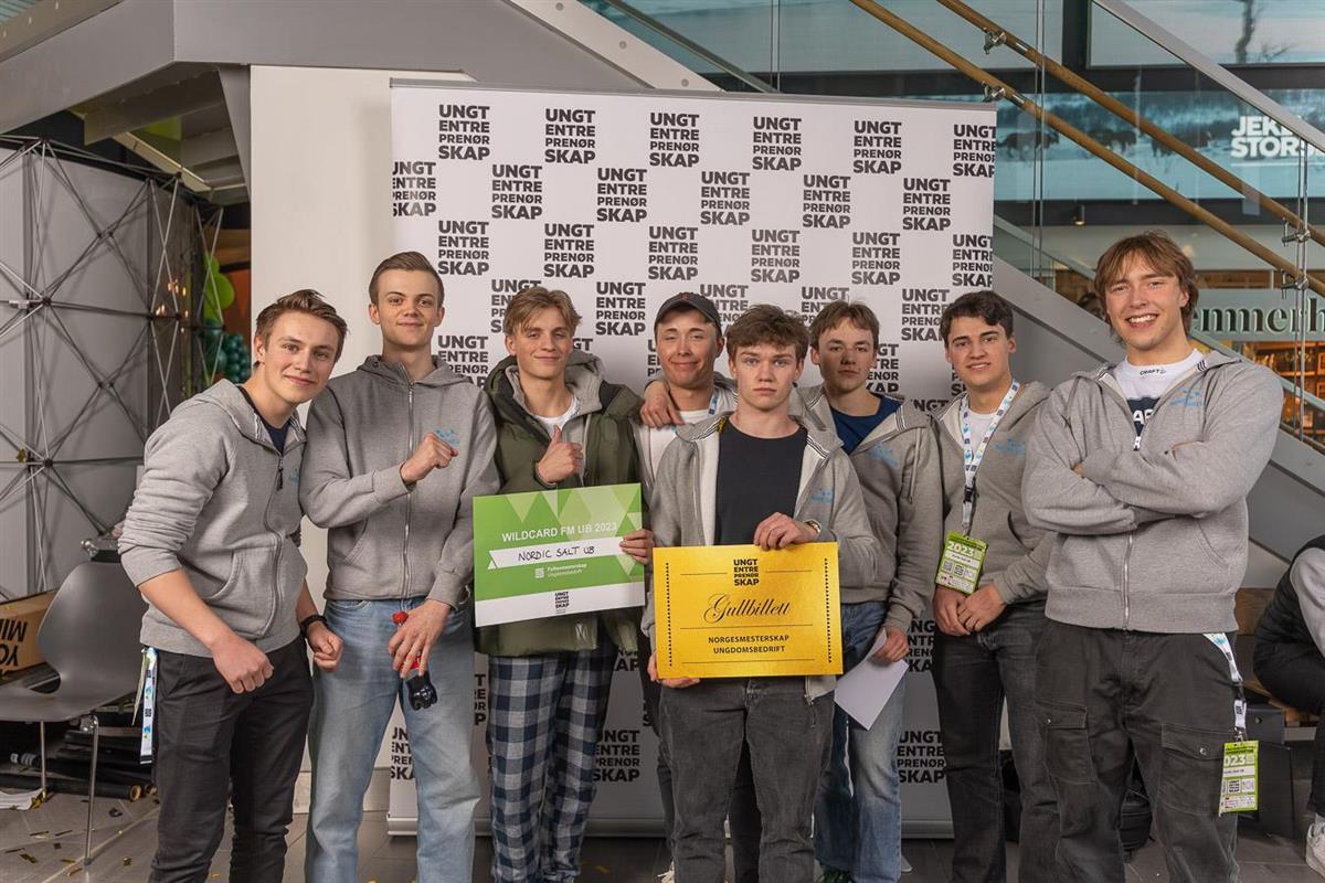 åtte gutter i ungdomsbedriften nordic salt oppstilt foran bakvegg for ungt entreprenørskap og holder en gull-billett til nm og et diplom - Klikk for stort bilde